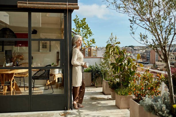 Relaxed senior woman standing on sunny deck with coffee