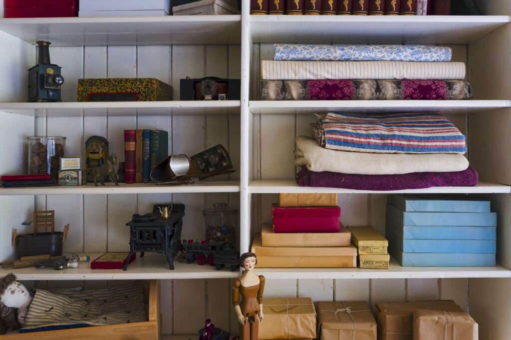 A vintage storage shelf filled with books, fabrics, antique items, and wrapped packages. 