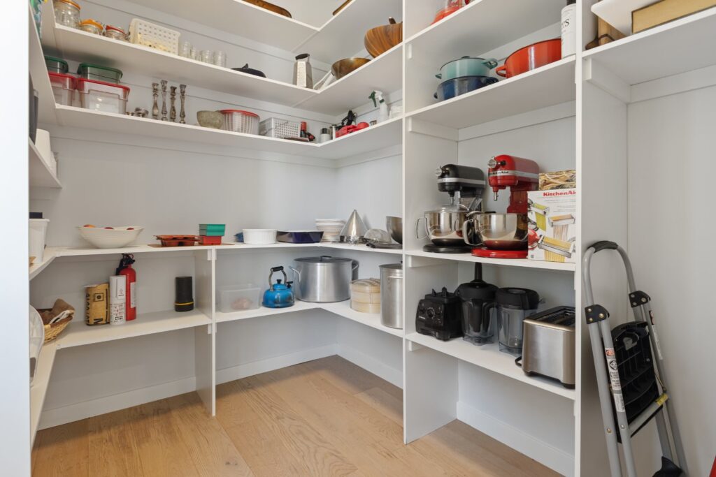 A well-organized pantry with white shelves holding kitchen appliances, cookware, and pantry essentials.